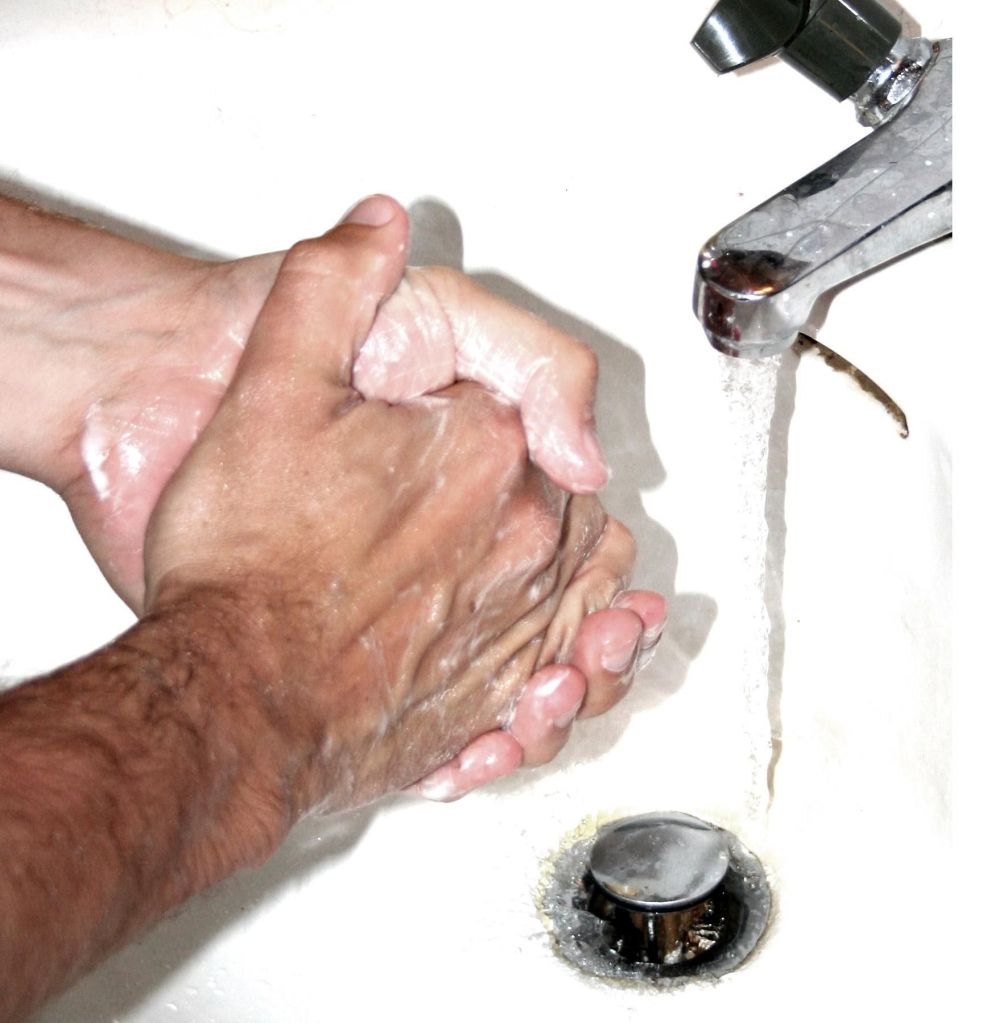 Close-up of two hands washing with soap under running water from a faucet.