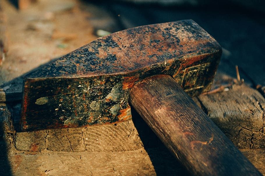 Close-up of a rusty hammer resting on a wooden surface, showcasing its weathered texture and worn wooden handle.