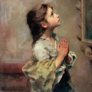 A young girl with long hair is kneeling in prayer, her hands clasped together and gaze directed upwards, wearing a white shirt and a colorful shawl.